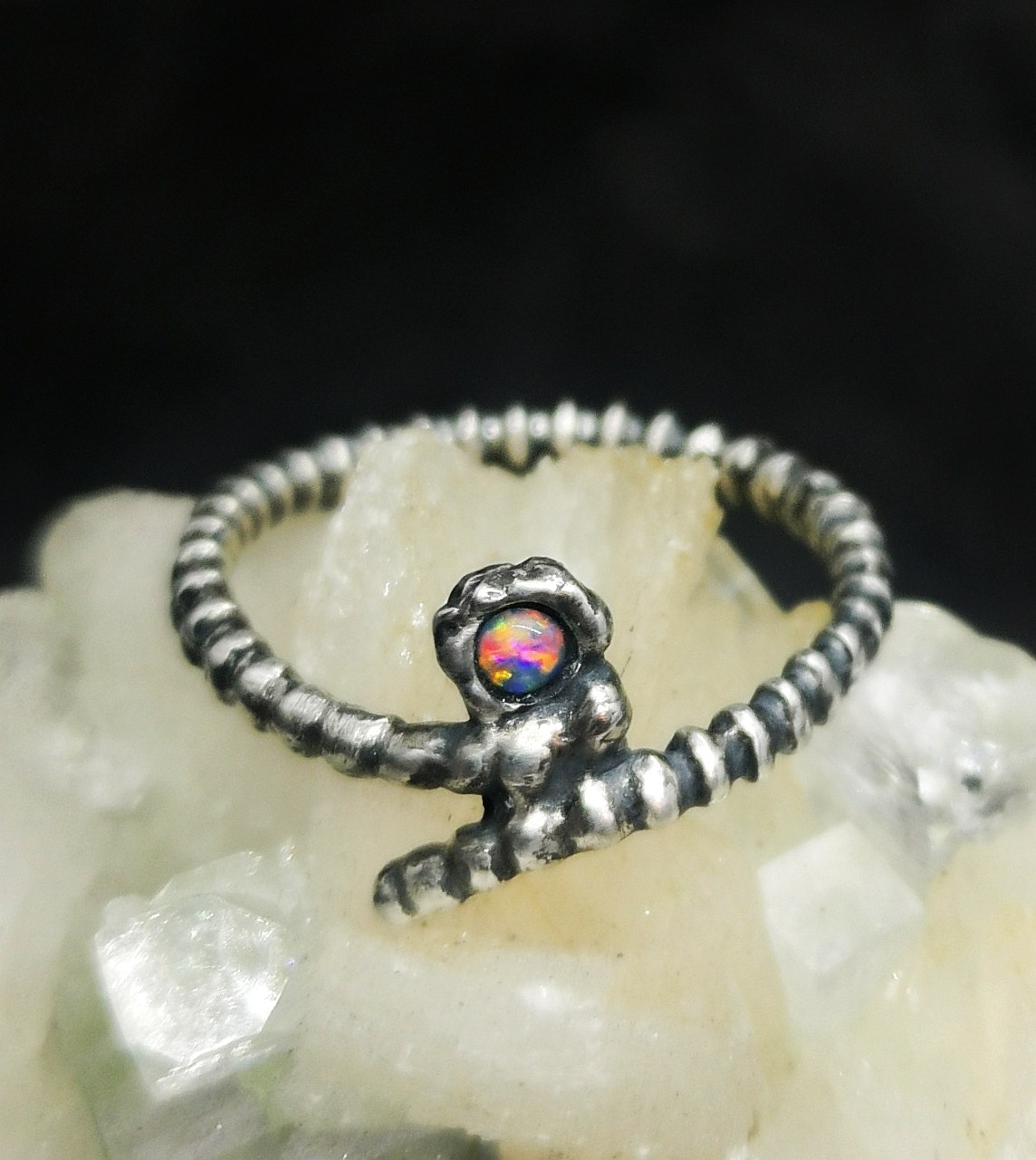 Gerillter Silber-Ring mit gebogenen Enden.  Im Ringkopf sitzt ein bunt schillernder Opal.